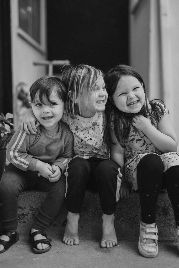 Three happy children sitting on a curb with their arms wrapped around each other